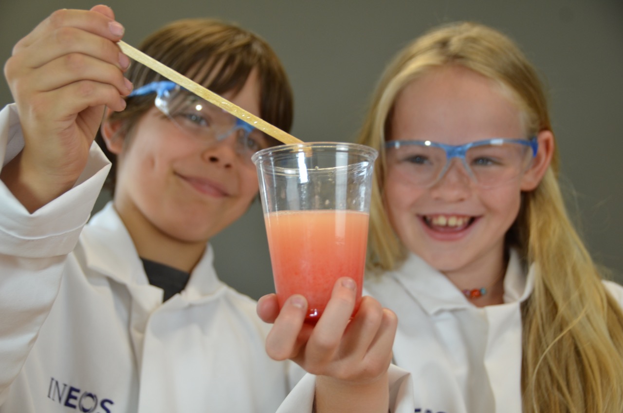 Zwei Kinder haben ein Becher mit orangener Flüssigkeit in der Hand